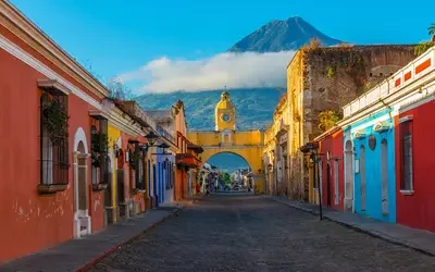 Cityscape of the main street and yellow Santa Catalina arch in the historic city center of Antigua at sunrise with the Agua volcano, Guatemala.