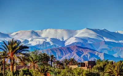 Snow-covered High Atlas Mountains overlooking a palm-filled valley in Morocco