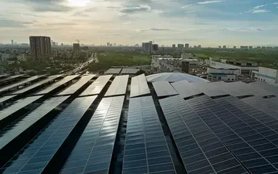 Solar panels in front of a city skyline and a sunny sky with clouds.