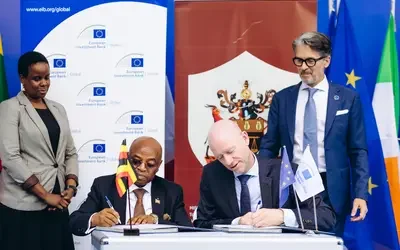Two people sitting at a table signing a document and two people standing next to them.