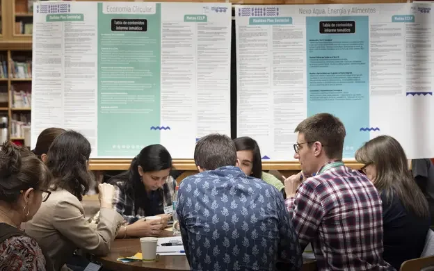 Participants gathered around a table during a workshop, reviewing and discussing planning materials displayed on presentation boards.