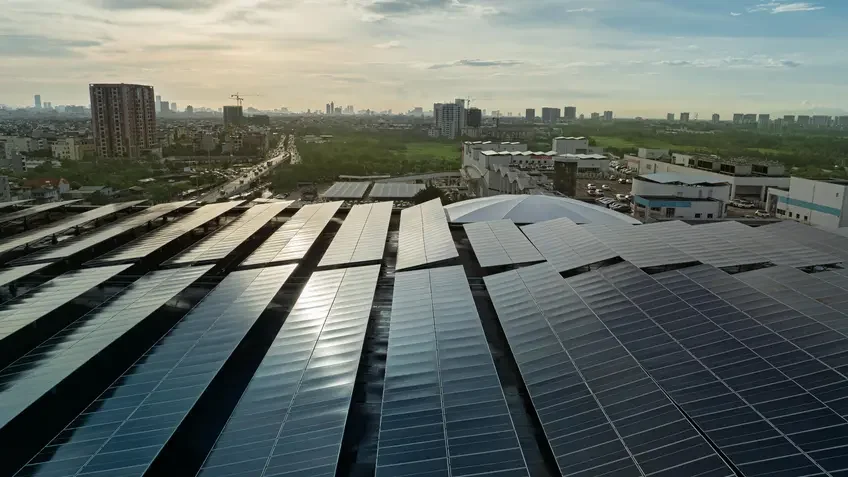 Solar panels in front of a city skyline and a sunny sky with clouds.