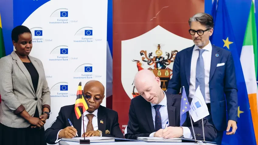 Two people sitting at a table signing a document and two people standing next to them.