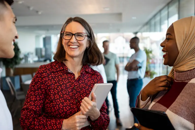 Three smiling people standing in discussion in an office environment