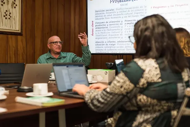 Participants take part in a workshop discussion during a scoping mission in Cuba in 2024, with laptops, meeting materials, and a presentation screen visible