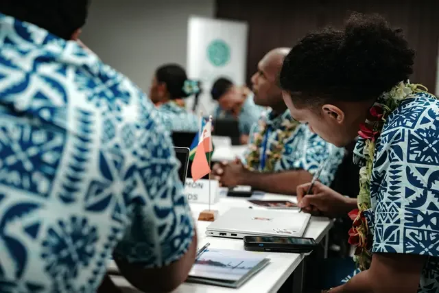 Participants attend a session of the NDCs 3.0 Forum for the Pacific in Samoa in 2024, seated at conference tables with laptops, documents, and country flags.