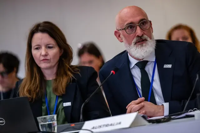 Participant speaks at a conference table during a Steering Committee Meeting session in Denmark, 2026, with microphones, laptops, and meeting materials visible.