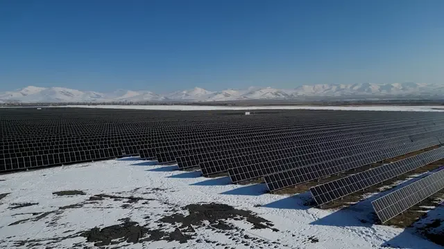Rows of solar panels at the Masrik-1 Solar Facility in Armenia, with snow-covered mountains in the distance.