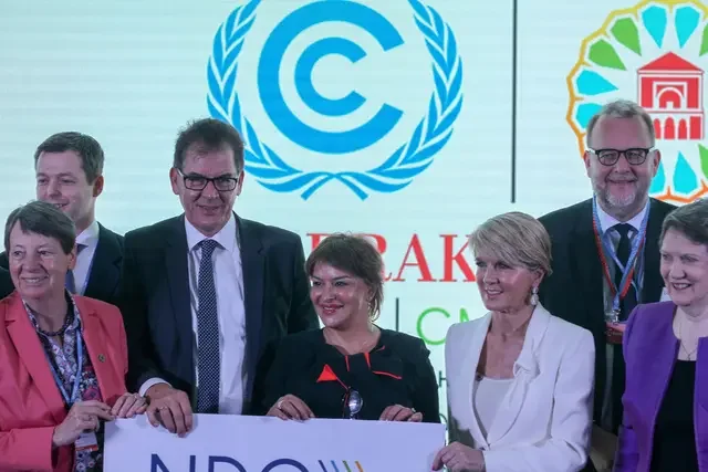 Participants gather for a group photo during the launch of the NDC Partnership in Morocco in 2016, holding a sign with the NDC Partnership name in front of a large display featuring climate conference branding and logos.